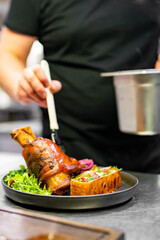 chef hand cooking Baked Pork knuckle with vegetables on plate in kitchen