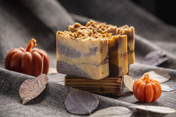 Natural soap with the aroma of pumpkin pie for a cozy autumn atmosphere on a dark background with yellow dry leaves and pumpkin shaped candles