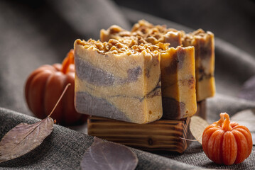 Natural soap with the aroma of pumpkin pie for a cozy autumn atmosphere on a dark background with yellow dry leaves and pumpkin shaped candles