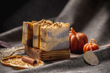 Natural soap with the aroma of pumpkin pie for a cozy autumn atmosphere on a dark background with yellow dry leaves and pumpkin shaped candles