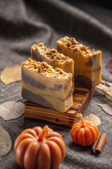 Handmade fragrant natural soap and pumpkin shaped candles on a dark background with yellow dry leaves to create a cozy atmosphere . Beautiful autumn postcard