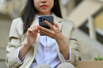 Businesswoman sitting on stairs outside office building and texting messages, chatting in social on smartphone