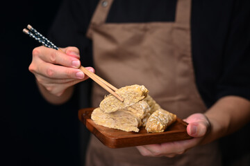 Closeup view man holding Tempeh with bamboo chopsticks. Vegan appetizers, traditional Indonesian soy product