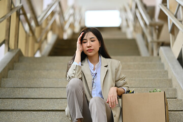 Fired businesswoman sitting hopelessly sitting on stairs of a business building. unemployment, depressed and fired from job