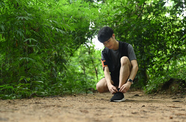 Full length of male runner tying shoes laces, getting ready for trail run in forest. Sports, adventure and healthy lifestyle
