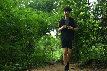Shot of young sporty man in sportswear running in green forest. Sports, adventure and healthy lifestyle