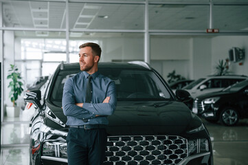 Handsome car dealership worker is with electric vehicle