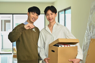 Happy asian gay couple holding cardboard box and sowing key of new home. LGBTQ, relocation and real estate property