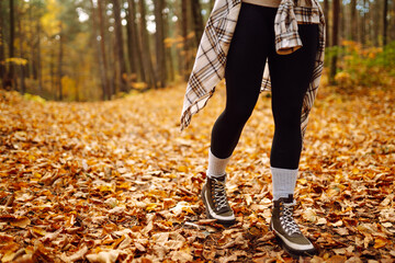 Woman's legs in boots in autumn foliage. Leaf fall. A woman tourist walks through fallen leaves in...