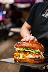 waiter hands hold a plate with a very big cheeseburger in pub