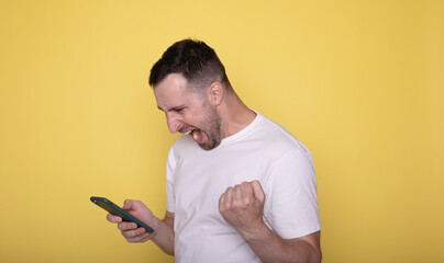Handsome smiling excited man holding mobile phone posing on yellow studio background. Celebrate, win gesture.