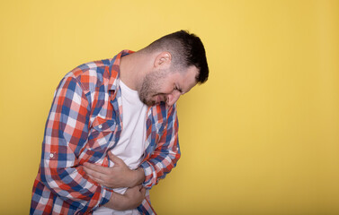 A man touching his stomach on yellow background with copy space. Stomach pain and others stomach disease concept.