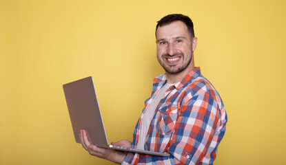 Amazed smiling handsome young bearded man holding underarm laptop pc computer isolated on yellow background.