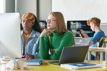 Schoolgirls working with online presentation on computer while sitting at desk in the classroom