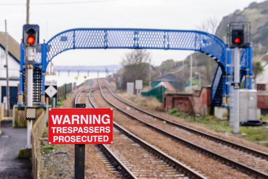 Warning sign and a pedestrian footbridge over railway tracks.
