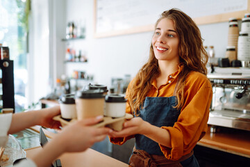 Takeaway food concept. A beautiful female barista gives to-go coffee to a client. Owner of a small business, a coffee shop,  behind the bar. Business concept.