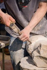 Stone mason carving a circular column with hammer and chisel