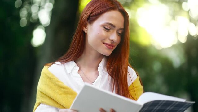 Close up portrait of beautiful girl preparing for exam studying and reading notebook at green park Pretty student make notes while having distance remote education outdoors 