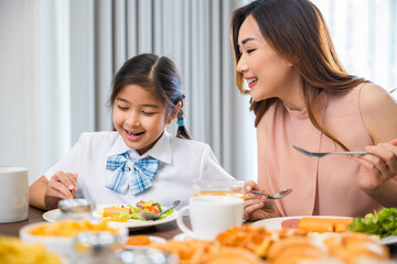 Asian family breakfast. smiling mother and child daughter having breakfast on food table, Healthy food at home before go to school, Mom and little preschooler have fun eating meal together