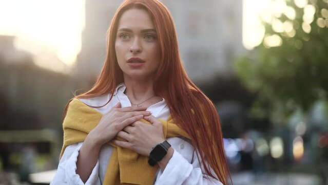 Worried red hair young woman walking down the urban street while has panic heart attack hold hand on chest and try to calm down alone Anxious female with mental health problem outdoors