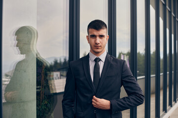 A CEO dressed in a sleek black suit stands confidently at the entrance of a modern corporate building, awaiting the start of the workday in the bustling urban environment.