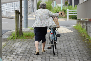 住宅地の道路で自転車を押して歩くシニア女性の姿