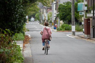 夏の昼の静かな住宅街の道路で自転車を乗っているシニア女性の姿