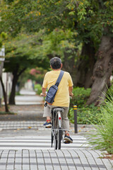 夏の昼の住宅街で自転車を乗っているシニア男性の後姿
