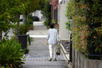 夏の昼の静かな住宅街で歩く一人のシニア女性の姿