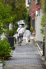 Fototapeta na wymiar 夏の昼の住宅街で自転車を乗っているシニア男性と散歩しているシニア女性の様子