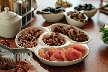 turkish breakfast table served, white dishes, wooden table, olives, nuts, dry figs, apricots, fruits, raisins, traditional morning