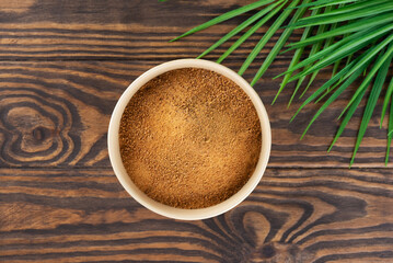 Brown cane sugar Panela in a bowl with palm branch on a wooden table.