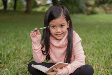 Asian girl thinking about studying in the garden. She is taking notes in a notebook.