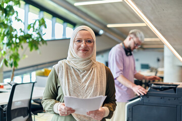 In a modern startup office, a business-minded Muslim woman wearing a hijab collaborates with her colleague, symbolizing diversity, empowerment, and success in the contemporary corporate world