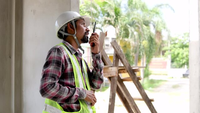 Small business contractor engineer architect foreman using walkie talkie instruct process of work from far distance in construction site area house building, Indian worker with mustache wearing helmet