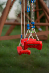 The empty red swing with ropes in the park