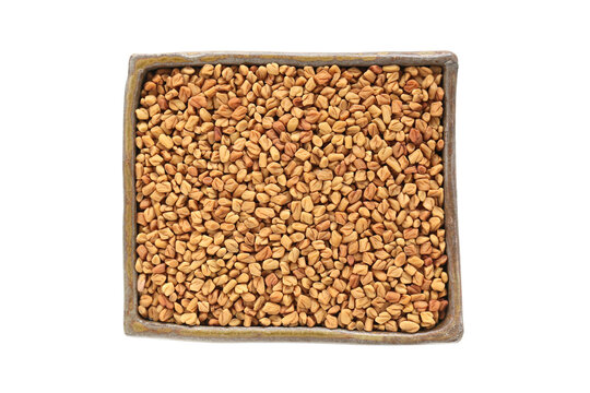 Top view of dried Fenugreek seeds, also called Methi Dana, in yellow color in ceramic bowl isolated on white background.