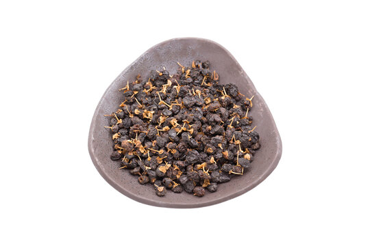 Black wolfberry, also called Black goji berry. These berries are used as herbal tea in traditional Chinese medicine. Dried herbs in clay dish, selective focus isolated on white background..