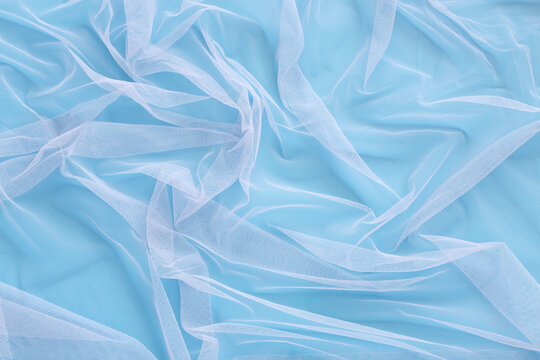 Wavy pattern of bright tulle fabric on soft colorful blue background. Abstract light chiffon, clean beautiful net cloth with wrinkle mesh lace texture loosely draped to make design patterns. .
