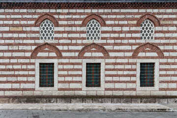 External wall of 16th century Selman Aga Mosque in Uskudar, Istanbul, Turkey. The wall is made of red brick and has two rows of arched perforated stucco and wrought iron windows