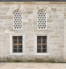 Two perforated arched stucco windows and two windows with wrought iron bars on a weathered brick external wall in Mihrimah Sultan Mosque in Uskudar, Istanbul, Turkey