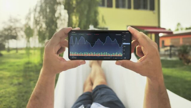 pov of person on the hammock trading online on smartphone app,point of view of man's hands holding smart phone watching stock market data realtime in the home garden