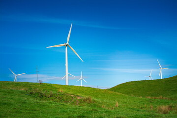 Landscape of green hills and turbine windmill field against blue sky and white clouds. Concept of alternative energy and sustainability. Palmerston North, New Zealand