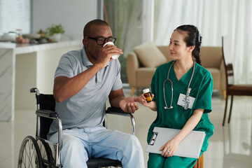 Obraz premium Sick patient in wheelchair taking pills and drinking water