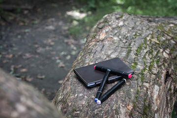 A brown leather notebook and black markers lie on a fallen tree in the forest. Image about creativity, for your creative design or illustrations.
