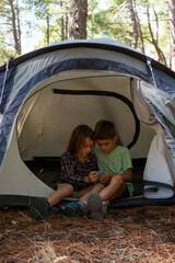 Two children looking at their phones inside a tent