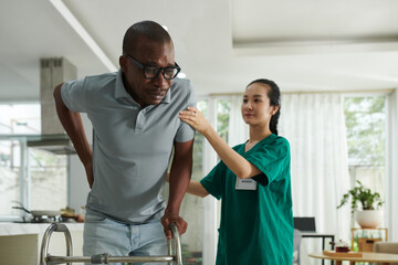 Fototapeta premium Patient crying from acute pain in lower back when trying to make steps with walker for the fist time