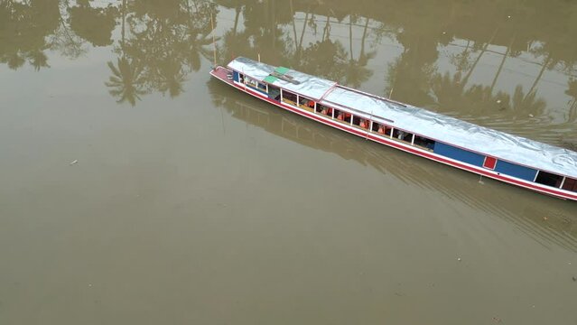Aerial closeup of a traditional slow boat with tourists cruising along the Mekong River in Luang Prabang, Laos. 