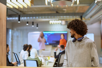 In a modern office environment, an African American young entrepreneur with headphones engages in work, while in the background, his dedicated colleagues exemplify teamwork and collaboration