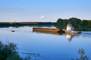 Fototapeta na wymiar A tug with a barge floats along the river. Cargo transportation by river transport